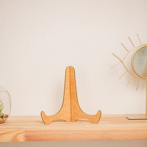 May include: A wooden display stand with a simple design, perfect for showcasing small items like photos, artwork, or figurines. The stand is made of natural wood and has a light brown color.
