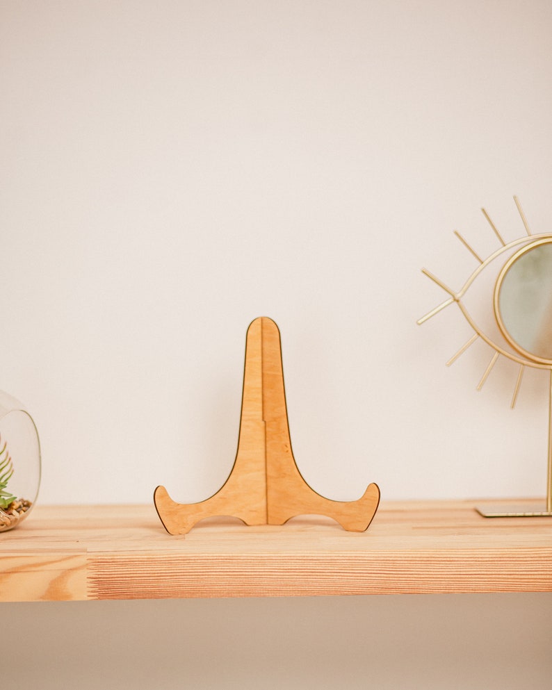 May include: A wooden display stand with a simple design, perfect for showcasing small items like photos, artwork, or figurines. The stand is made of natural wood and has a light brown color.