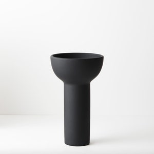 May include: A black ceramic vase with a wide, rounded opening and a tall, cylindrical base.