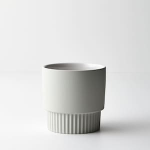 May include: A white ceramic planter with a ribbed base. The planter is a simple, modern design.