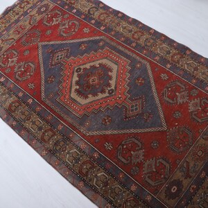 May include: A rectangular, vintage-style rug with a central diamond pattern in shades of red, blue, and brown. The rug features intricate geometric designs and a distressed appearance, suggesting it is an antique or a well-loved piece.