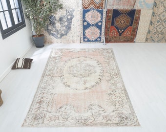 Op de afbeelding: Een lichtroze en crèmekleurig vintage tapijt met een bloemenpatroon. Het tapijt heeft een verweerde look en is perfect om elke kamer een vleugje bohemian stijl te geven.