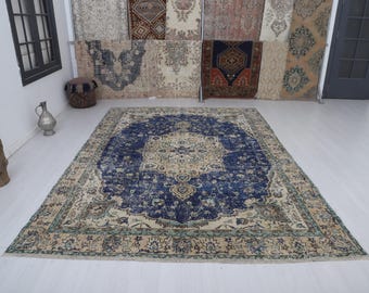 May include: A large, rectangular rug with a central medallion design in shades of navy blue and beige. The rug features an intricate, traditional pattern with a distressed, vintage look. The border is a lighter beige with hints of green.