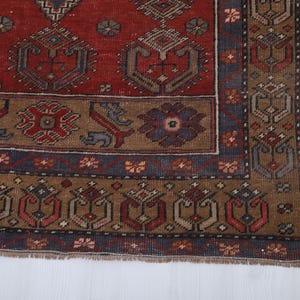May include: Close-up of a section of a vintage rug with a detailed geometric pattern. The rug features a rich color palette of red, brown, and blue. The design includes repeating motifs and a decorative border, showcasing traditional craftsmanship.