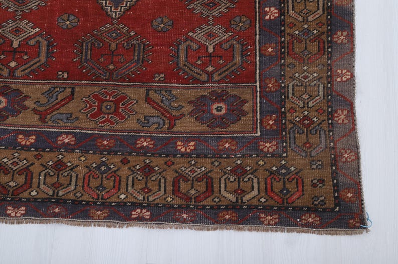 May include: Close-up of a section of a vintage rug with a detailed geometric pattern. The rug features a rich color palette of red, brown, and blue. The design includes repeating motifs and a decorative border, showcasing traditional craftsmanship.