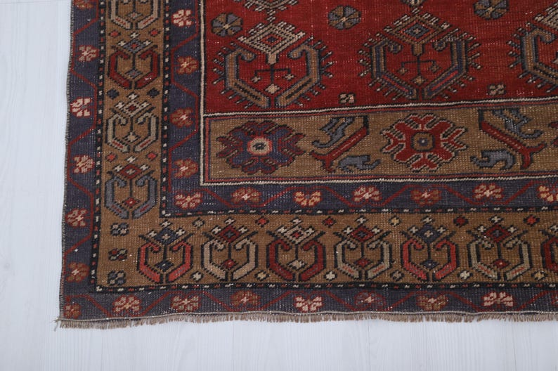 May include: Close-up of a section of a vintage rug with a detailed geometric pattern. The rug features a rich color palette of red, brown, and navy blue. The design includes repeating floral and geometric motifs, with a fringed edge.