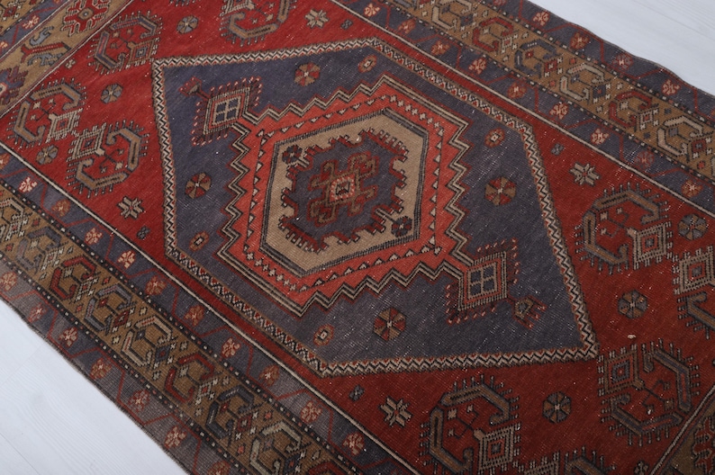 May include: A rectangular rug with a central diamond pattern in shades of red, blue, and brown. The rug features intricate geometric designs and a border with repeating motifs. The rug's color palette and patterns suggest a traditional or vintage style.