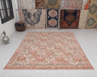 May include: A vintage rug with a cream background and a repeating diamond pattern in shades of pink, brown, and green. The rug has a distressed look and a frayed border.