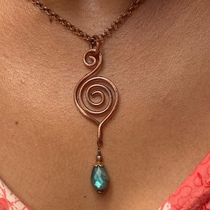 May include: A copper wire pendant necklace featuring a hand-formed spiral design suspended from a matching copper chain. A single teardrop-shaped blue gemstone bead with a metallic cap hangs from the bottom of the wire-wrapped spiral element.