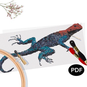 May include: Cross-stitch design of a lizard with a red head and blue body. The lizard is on white fabric, with embroidery threads and a wooden hoop. The image includes the text "PDF".