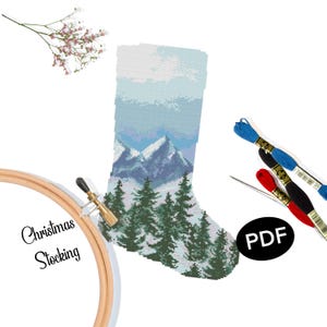 May include: A cross-stitch Christmas stocking depicting a winter mountain scene with evergreen trees in shades of blue, white, and green. The image includes embroidery floss, a needle, and the text "Christmas Stocking" and "PDF".