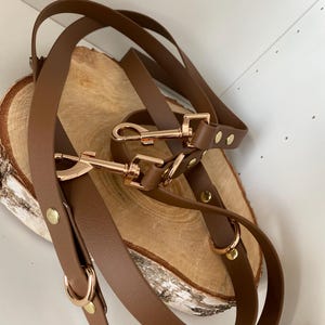 Peut inclure: Deux laisses pour chien en cuir marron avec des accessoires dorés. Les laisses sont reliées entre elles et ont un anneau en D et un mousqueton à chaque extrémité.