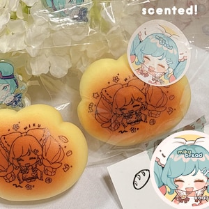 May include: A collection of themed merchandise featuring a cartoon character. Includes two cloud-shaped squishies with a character design, a keychain, and a postcard. The squishies are yellow and orange, with a printed character illustration. The postcard features a character illustration.