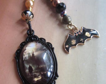 Può includere: Una collana con due ciondoli appesi a cordini neri. Un ciondolo è una cornice ovale nera contenente una scena paesaggistica scura con una figura. Il secondo ciondolo è un pipistrello in smalto nero con stelle dorate e dettagli fantasma.