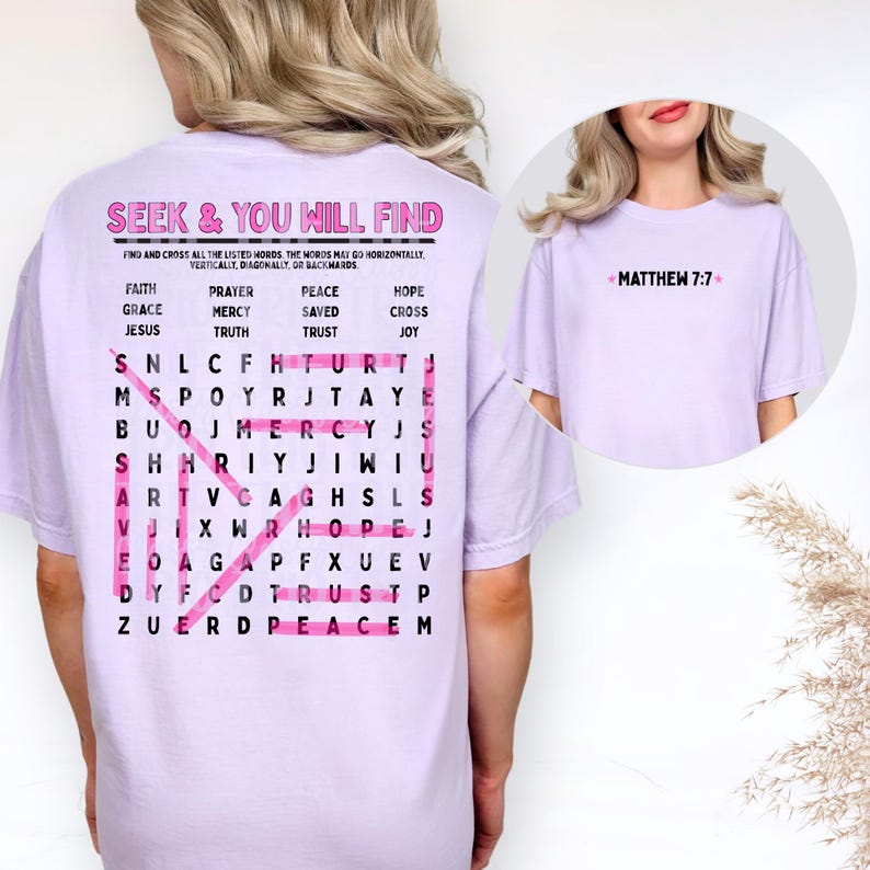 May include: A light purple t-shirt featuring a word search puzzle on the back with the text SEEK & YOU WILL FIND and a list of words including FAITH, GRACE, JESUS, PRAYER, MERCY, TRUTH, PEACE, SAVED, TRUST, HOPE, CROSS, and JOY. The front has MATTHEW 7:7.