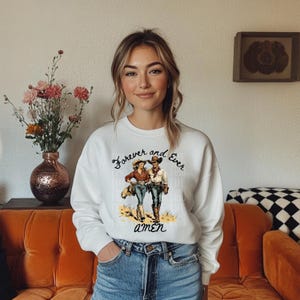 Puede incluir: Sudadera blanca con un gr&aacute;fico de un vaquero y una vaquera con el texto "Forever and Ever Amen".