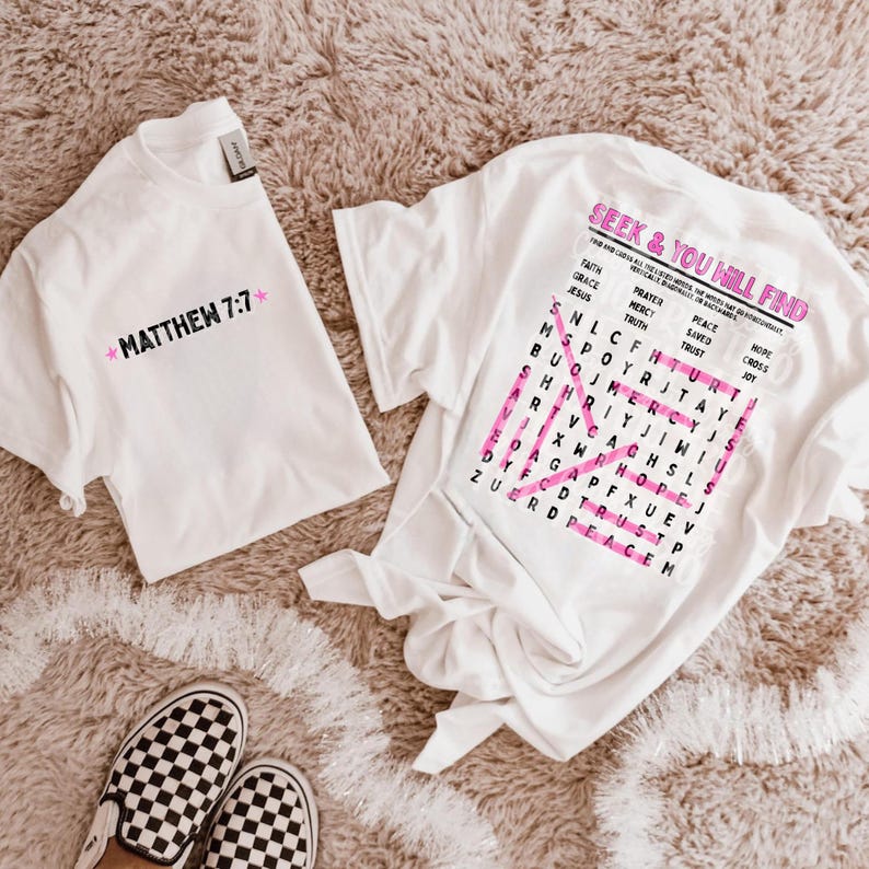 May include: Two white t-shirts. The left shirt features the black text "MATTHEW 7:7" flanked by two pink stars. The right shirt displays the pink text "SEEK & YOU WILL FIND" above a word search grid with pink highlighted words and a large pink X.