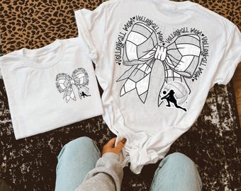 May include: Two white t-shirts featuring a black and white volleyball bow design. The larger shirt has the text "Volleyball Mom" repeated around the bow. The smaller shirt has a smaller bow design.