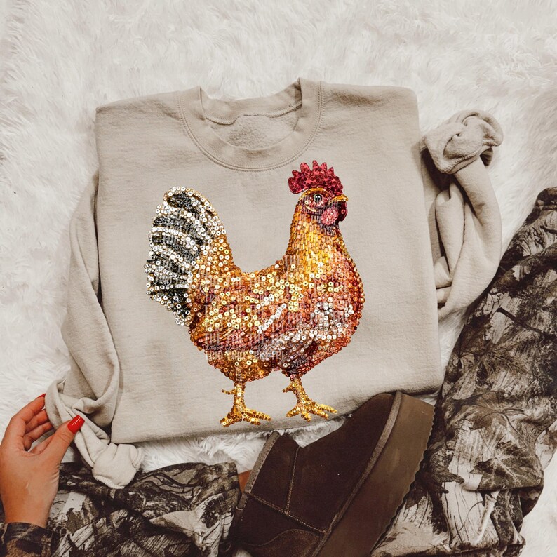 May include: A beige sweatshirt with a sequined rooster design. The rooster is brown, gold, and black with a red comb.