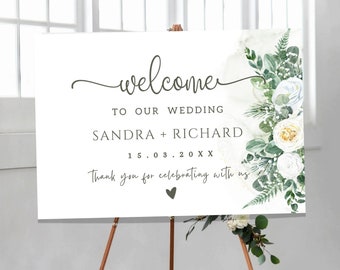 May include: White wedding welcome sign with green foliage and white flowers. The sign reads "Welcome to our wedding Sandra + Richard 15.03.20XX Thank you for celebrating with us".