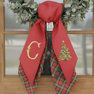 May include: Red Christmas door scarf with a gold embroidered letter "C" and a Christmas tree design. The scarf has a plaid pattern on the bottom. A festive holiday decoration.