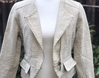 May include: A cream-colored, short-sleeved jacket with a zipper closure and a textured fabric. The jacket has two pockets on the front.