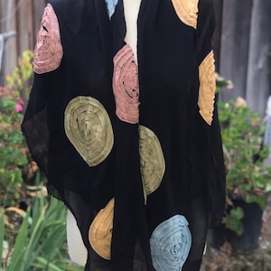 May include: A black sheer scarf with colorful, circular, fabric appliques. The appliques are in shades of blue, green, and pink.