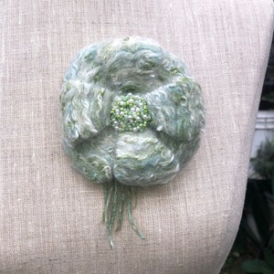 May include: A green and white felted flower brooch with a center of green and white beads.