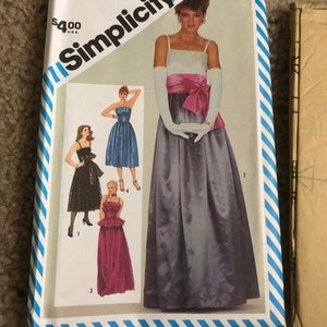 May include: Simplicity sewing pattern number 6211 for a long evening gown. The pattern includes four different styles of gowns, including a white gown with a pink sash, a blue gown, a black gown with lace, and a pink gown. The pattern is for size 12 miss.