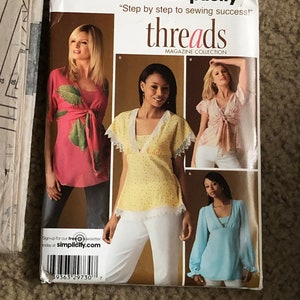 May include: A Simplicity Threads magazine pattern for sewing tops. The pattern includes three different styles of tops: a yellow top with white lace trim, a pink top with a tie at the neck, and a light blue top with long sleeves. The pattern is for sizes 8, 10, 12, 14, and 16.