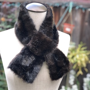 May include: A brown faux fur scarf with a long, narrow shape. The scarf is tied in a knot around a white mannequin's neck.