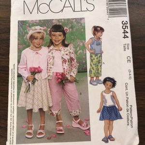 May include: A sewing pattern for children's clothing. The pattern includes three different styles: a pink and white striped dress with a pink cardigan, pink and white striped pants with a pink cardigan, and a blue and white polka dot skirt with a white tank top. The pattern is for sizes 3-4-5. The pattern is from McCall's.