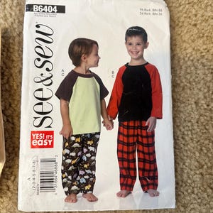 May include: A sewing pattern for children's pajamas. The pattern includes two different styles of pajamas, one with a red and black plaid pattern and the other with a black and white animal print. The pattern is labeled "B6404" and "see&sew".
