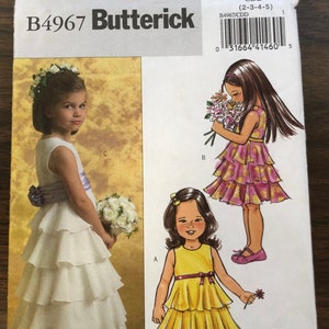 May include: A sewing pattern for a girl's dress. The pattern includes three different styles: a white dress with a sash, a yellow dress with a red sash, and a pink dress with a yellow sash. The pattern is for sizes 2-3-4-5. The pattern number is B4967.