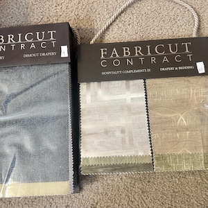May include: Two fabric sample books from Fabricut Contract. One features a blue-grey dimout drapery, the other showcases drapery and bedding in neutral tones. The text on the sample books reads "Solar Library" and "Hospitality Compliments IX".