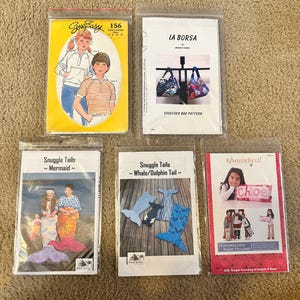 May include: Five different sewing patterns, including a shoulder bag pattern, a children's clothing pattern, and three patterns for snuggle tails. The patterns are printed on white paper and are enclosed in clear plastic bags.