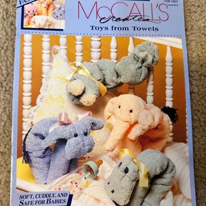 May include: A McCall's Creates pattern book for making toys from towels. The cover features a photo of four plush toys made from towels: a blue donkey, a pink elephant, a gray hippopotamus, and a blue and white striped elephant. The text on the cover reads "McCall's Creates Toys from Towels".