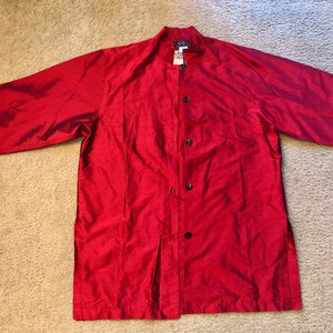 May include: A long-sleeved, red, button-up shirt with a mandarin collar. The shirt has a slight sheen and is made of a silky fabric. The label on the shirt reads "UCI".