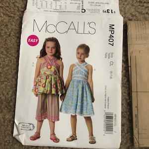 May include: A McCall's sewing pattern for children's clothing, featuring two girls modeling dresses and a top with pants. The pattern envelope is white with the McCall's logo and the word "EASY". The pattern number is MP407.