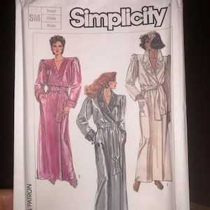 May include: Simplicity sewing pattern number 7186 for a long robe with a shawl collar and long sleeves. The pattern includes three different styles: a pink robe, a gray robe, and a white robe. The pattern is for sizes small, petite, and klein.