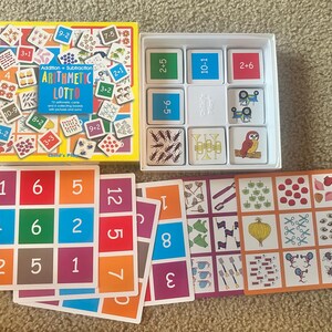 May include: A children's arithmetic lotto game with a yellow box and white container. The box reads "Addition + Subtraction Arithmetic Lotto". The game includes cards with numbers, addition, and subtraction problems, and picture cards.