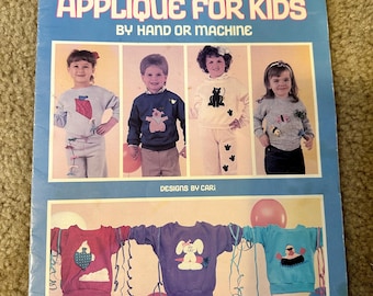 May include: A vintage craft leaflet titled "Appliqué for Kids by Hand or Machine." The cover features four children wearing colorful sweatshirts with appliqués of animals and other designs. The leaflet is from Leisure Arts Craft Leaflets and is numbered 1065. The price is $3.00.
