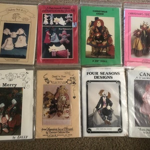 May include: A collection of eight doll-making patterns featuring various designs, including a Christmas tree topper, a whimsical doll, a clown doll, and a Santa doll. The patterns are printed on white paper with colorful illustrations and text.