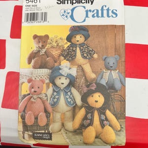 May include: A Simplicity Crafts sewing pattern envelope, number 5461, featuring illustrations of five different teddy bears. The bears are depicted wearing various outfits, including hats, vests, and bows. The text includes the brand name Simplicity Crafts, the pattern number 5461, and the designer name Elaine Heigl Designs.