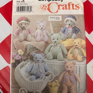 May include: A Simplicity Crafts sewing pattern envelope 5247 featuring illustrations of six different teddy bears in various outfits, including hats and jackets, with the text Simplicity Crafts and Elaine Heigl Designs printed on the front.