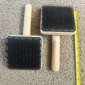 May include: Two square slicker brushes with light-colored wooden handles and black bristle pads. A yellow measuring tape is positioned next to the brushes, showing the brush head width is approximately 3 inches and the total length is 9 inches.