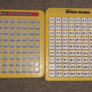 May include: Two yellow educational math tools. One is labeled "Magic Math Multiplication" and the other "Division Machine." Both have a grid of numbers for learning multiplication and division. The multiplication tool has a red label.