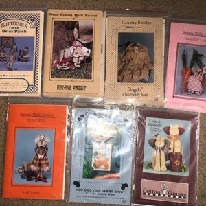 May include: A collection of nine craft patterns for making rag dolls and other crafts. The patterns feature various designs, including a bunny, a hare, a garden, and a pair of dogs. The patterns are printed on paper and are packaged in plastic bags.