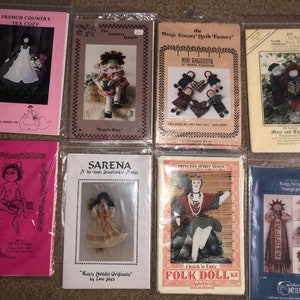 May include: Nine different doll-making patterns featuring various dolls, including a French Country Tea Cozy, a Southwest Angel, a Princess Spirit Moon, and a Raggy Stripp Hangups. The patterns are printed on white paper with colorful illustrations.