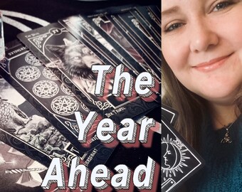 Op de afbeelding: Een vrouw glimlacht terwijl ze een tarotkaartlezing voor het komende jaar vasthoudt. De kaarten zijn zwart met zilveren accenten en bevatten afbeeldingen van wolven, manen en andere mystieke symbolen. De tekst "The Year Ahead" is geschreven in grote, vetgedrukte letters.